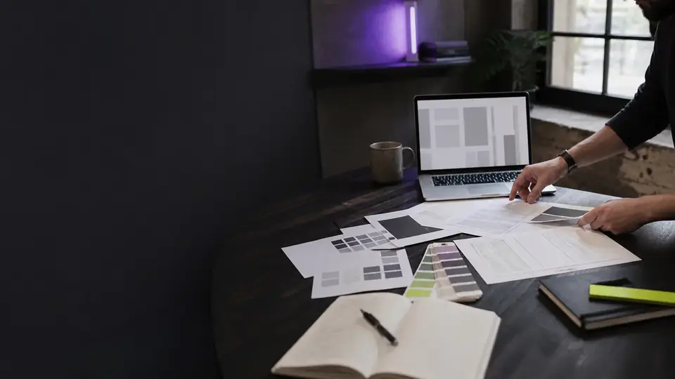 Page layouts, color swatches and notes spread beside a laptop on a studio table.