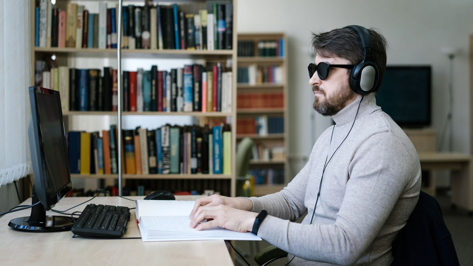 Man wearing headphones and dark glasses using a desktop computer with a screen reader
