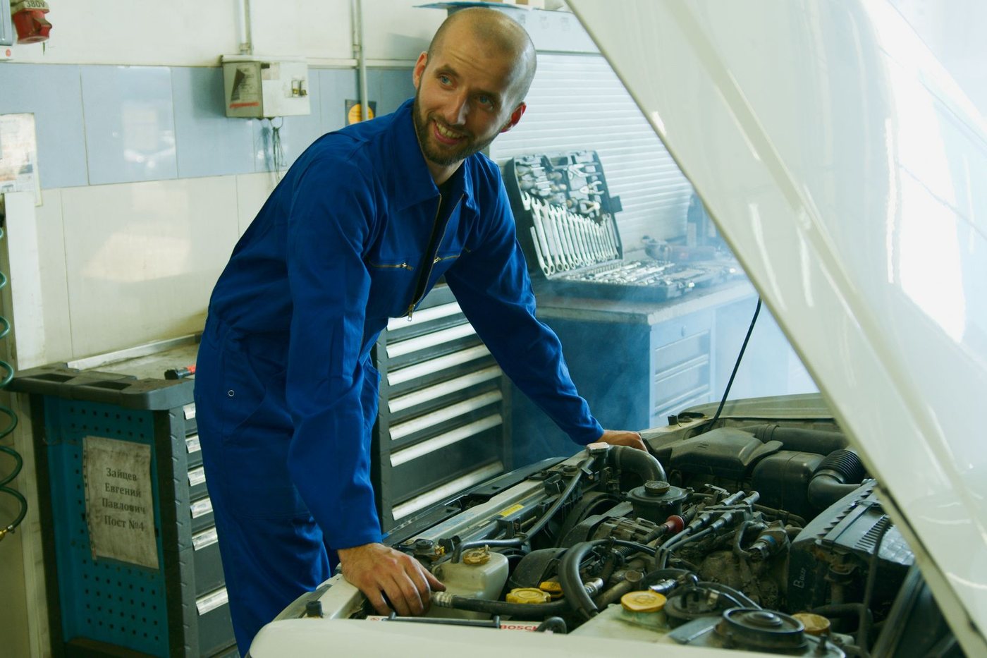 Mechanic leaning over an open hood while working in a bright repair bay