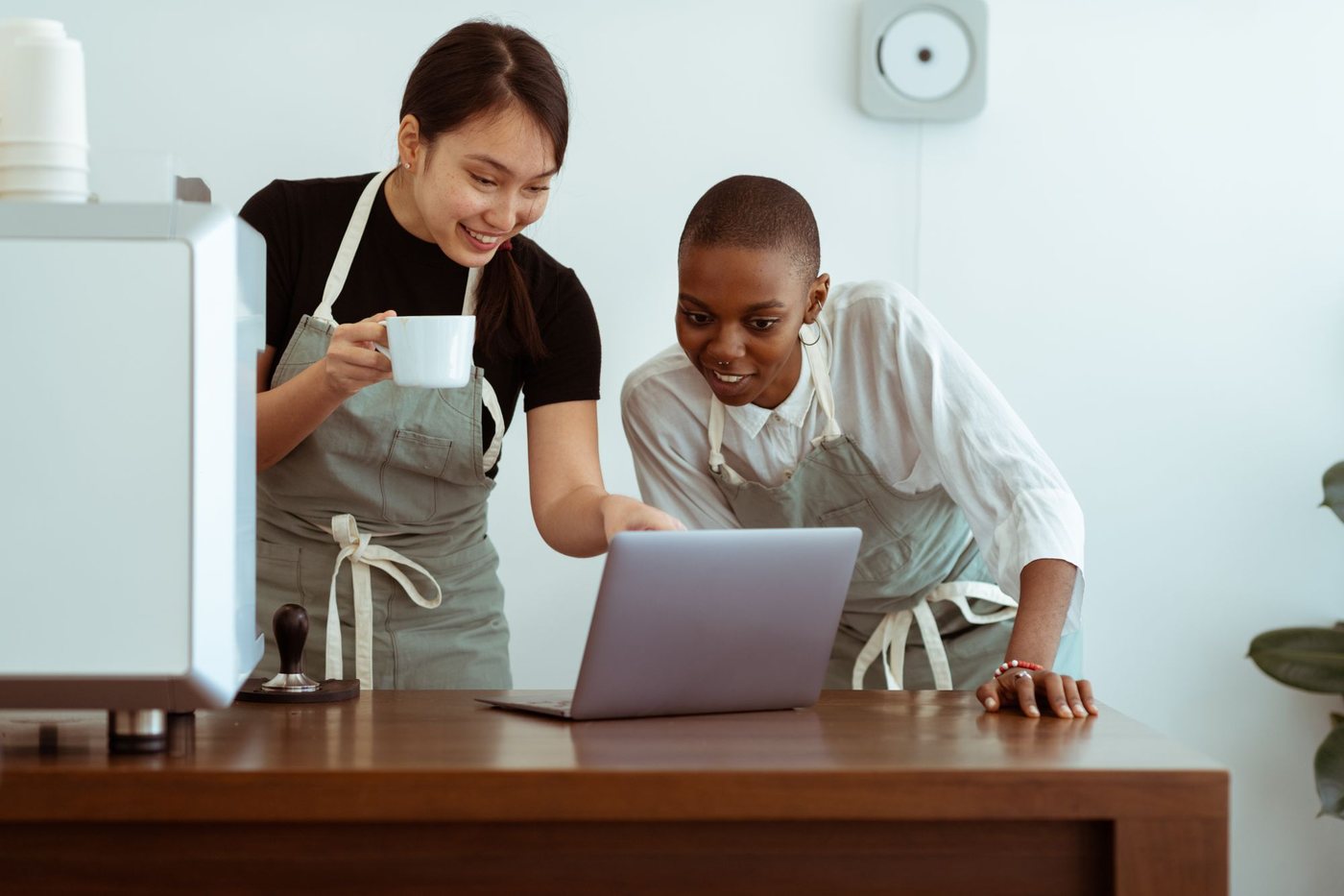 Two cafe employees in aprons looking at a laptop on the counter