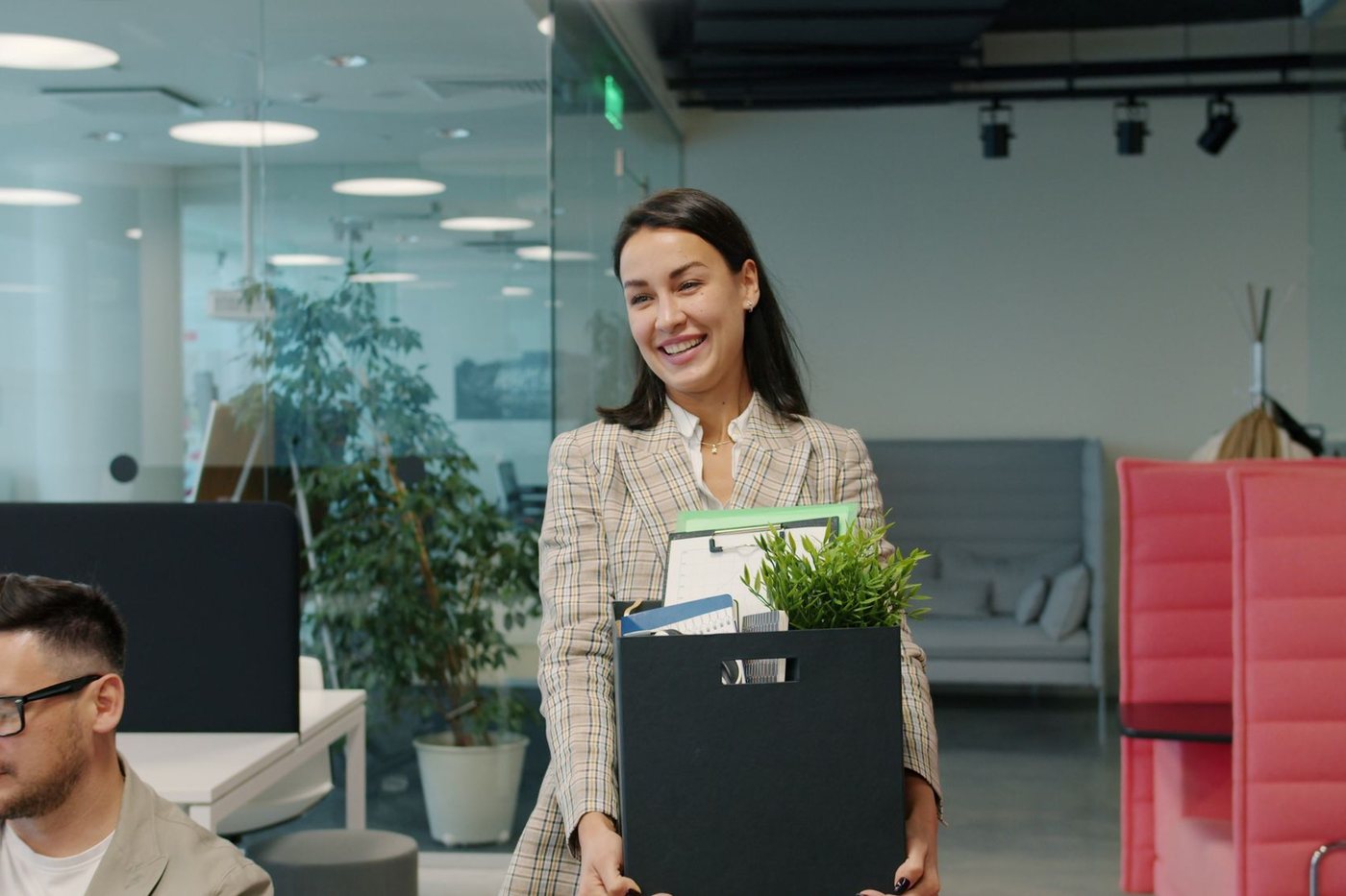 Smiling employee carrying a box of desk items through a bright office during a move