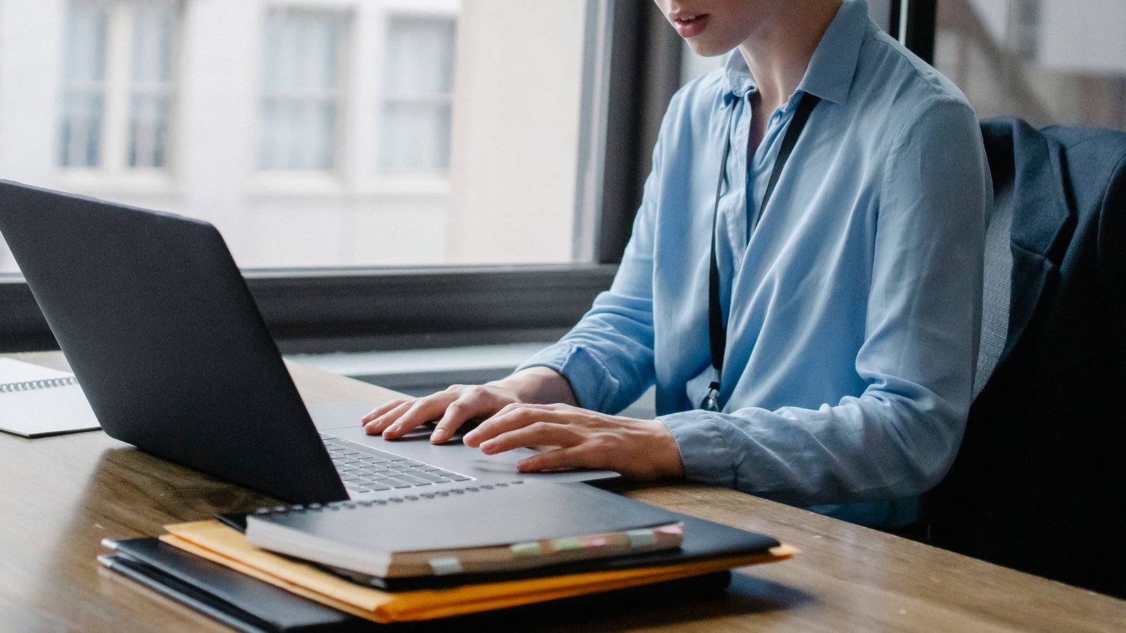 Office worker typing on a laptop beside a notebook and folders.