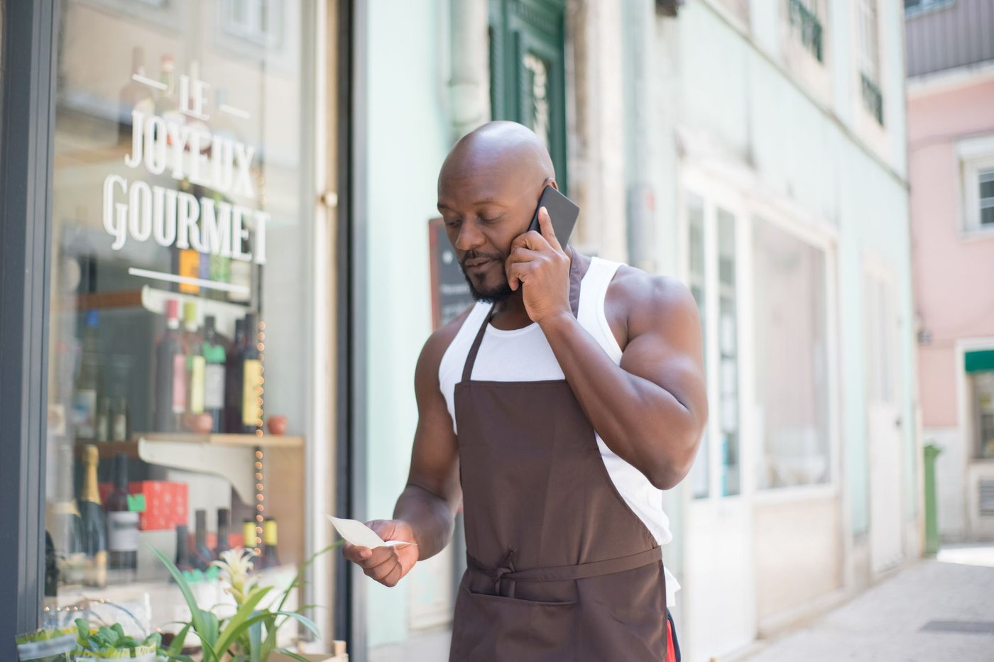 Shop owner in an apron taking a phone call in the doorway of his store