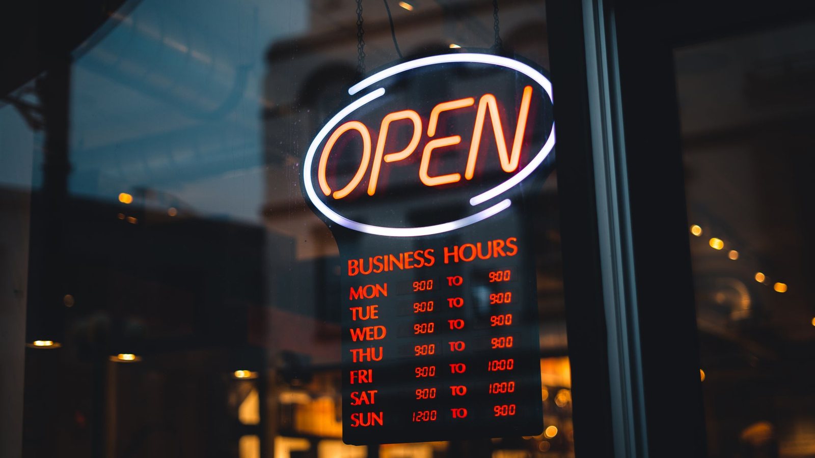 Neon open sign with posted business hours glowing in a shop window