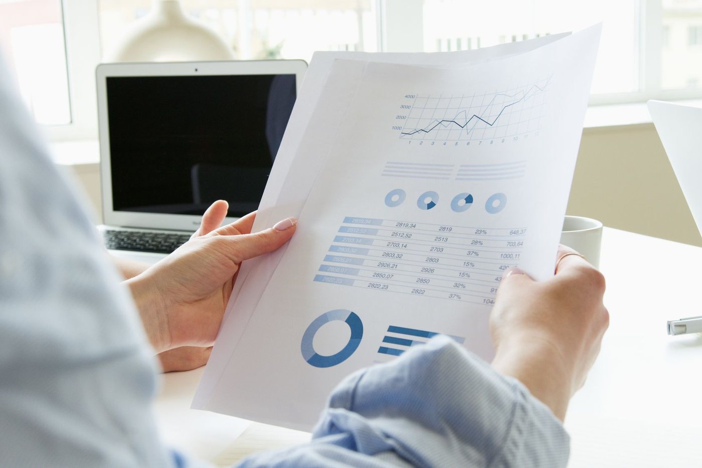Hands holding a printed marketing report with charts beside a laptop