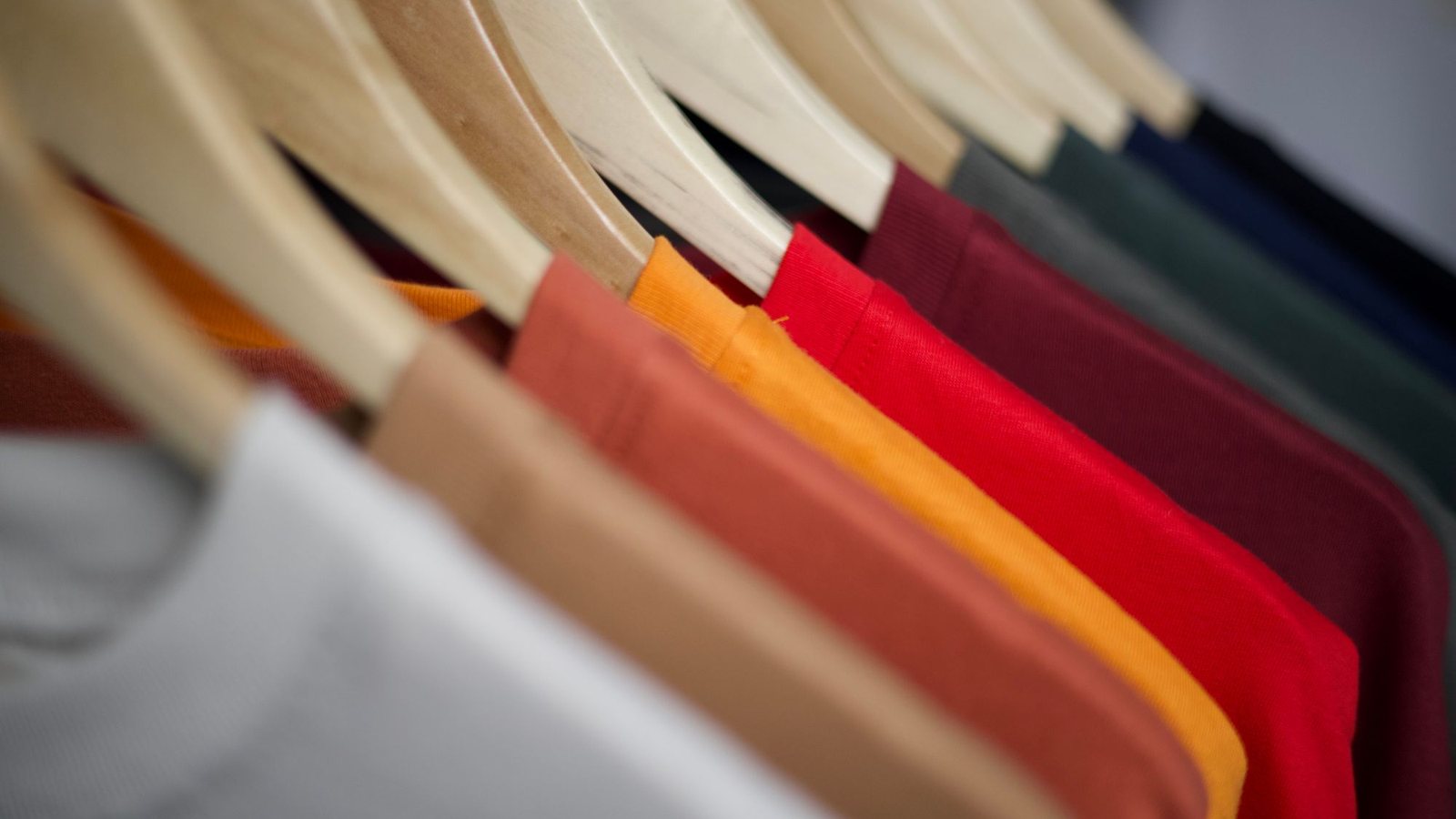 Row of plain t-shirts in different colors hanging on wooden hangers, the same product in several variants
