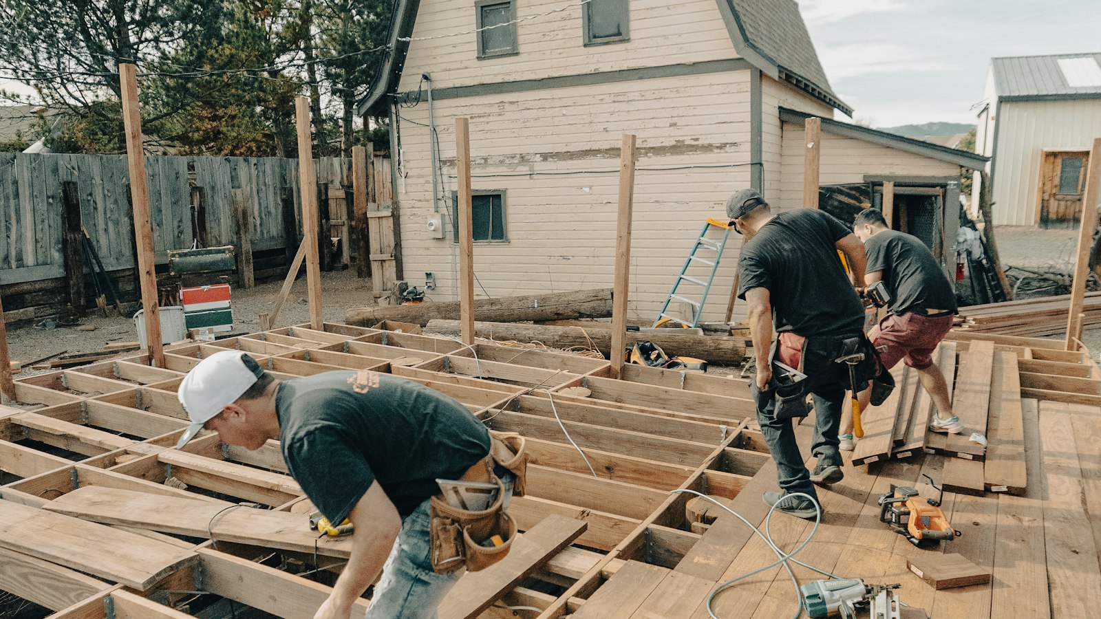 Two contractors framing a wooden backyard deck on a sunny day