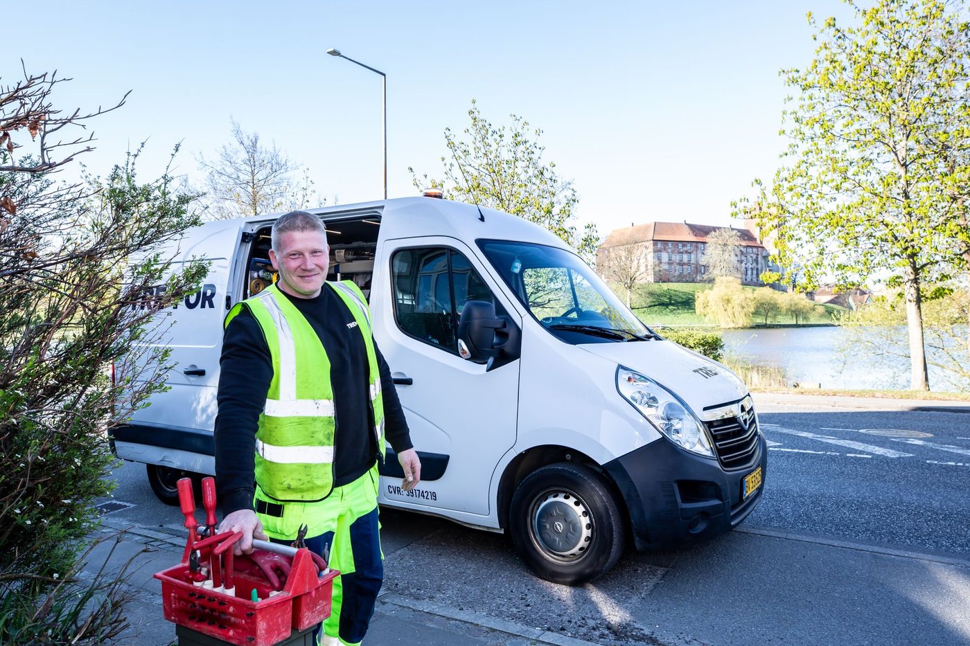 Service technician in a high-visibility vest carrying a toolbox beside a white work van
