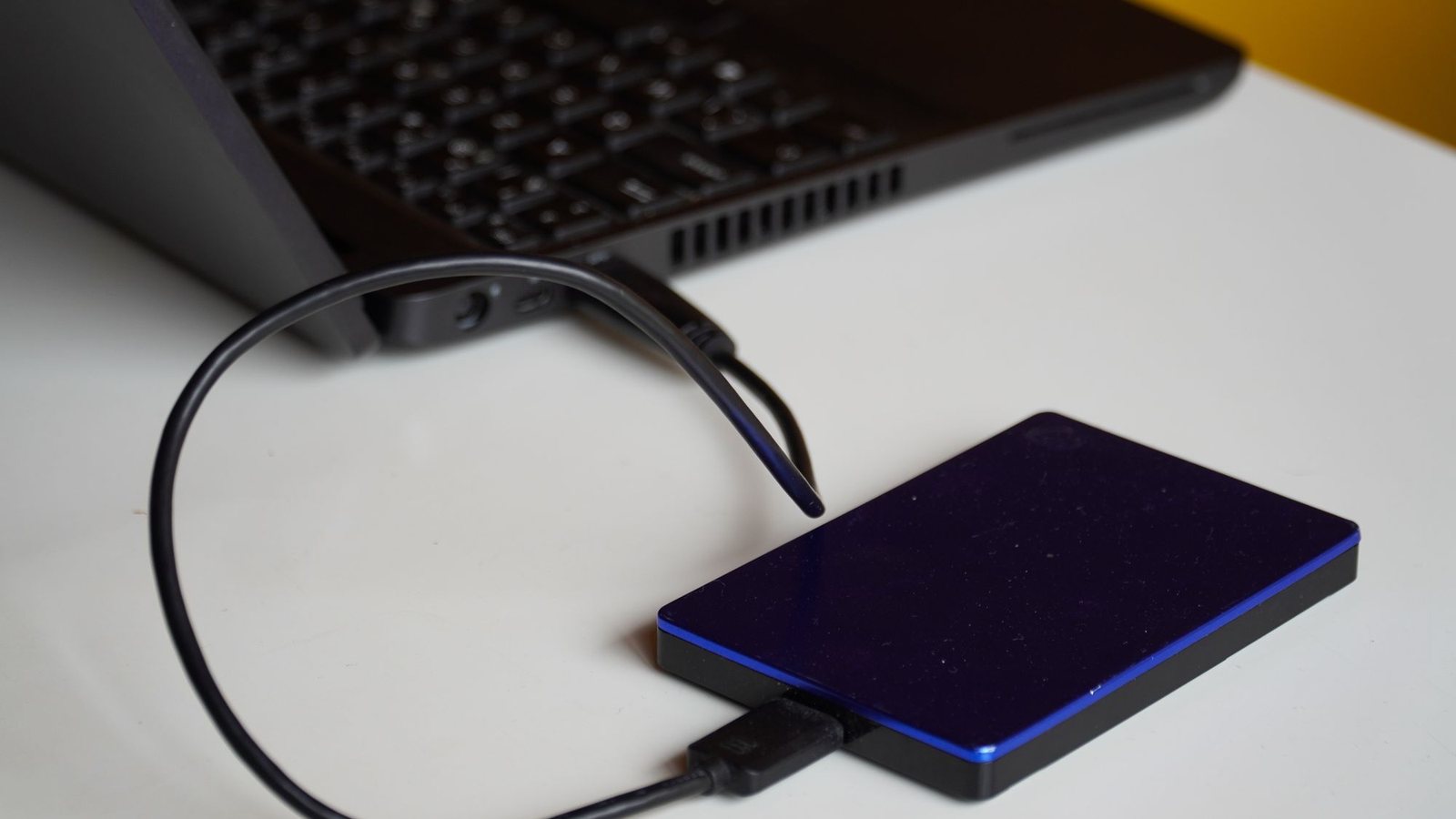 Portable external hard drive connected by cable to a laptop on a white desk