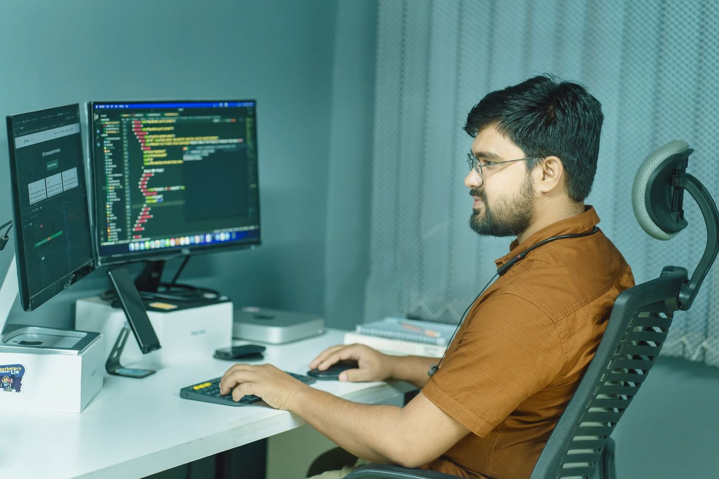 Developer working at a desk with a laptop and a monitor full of code